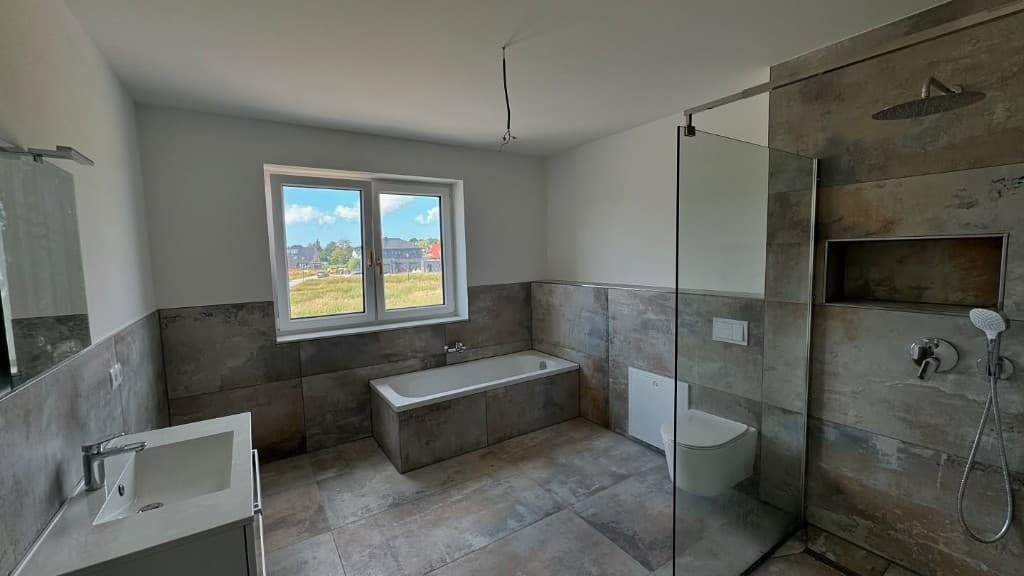 Bathroom with bathtub under window, stone-look tiles and walk-in shower area